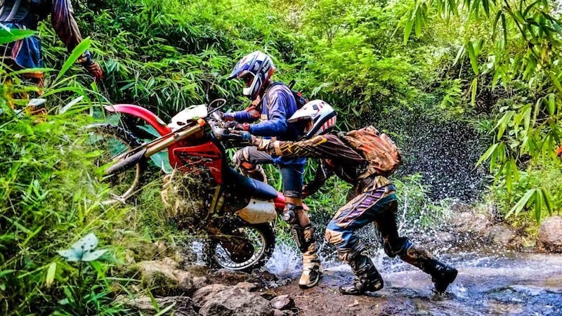 Travelers ride dirt bike through a stream